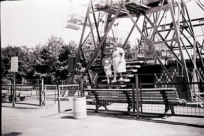 Mid-century amusement park ride with two children ascending a metal staircase. Black-and-white photo captures a classic swing...