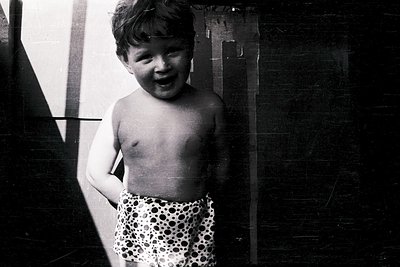Young boy in leopard-print swim trunks, smiling directly at camera. Black-and-white photo suggests mid-20th century (1950s–19...