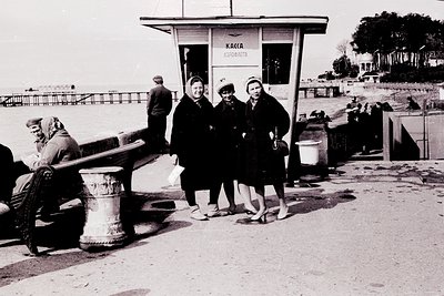 Black-and-white seaside photo: three women in 1960s-era dresses pose at a ticket booth labeled "Каса Експлоатация" (Exploitat...