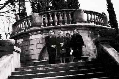 Four individuals pose on a grand stone staircase with balustrade, likely mid-20th century. Men wear suits, women in structure...