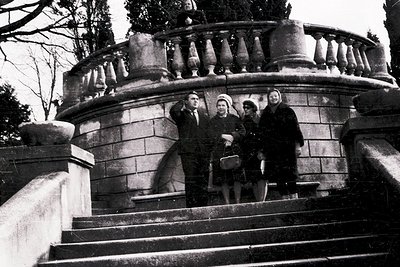 Black-and-white photo of four individuals posing on a grand stone staircase with balustrade, likely 1950s–1960s. Formal attir...