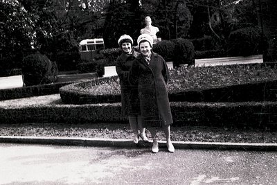 Two women pose on tiered park steps beside a sculpted tree, mid-20th century. Formal attire suggests a public event or offici...