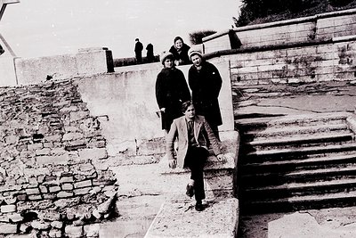 Four individuals pose on a stone staircase in a mid-20th-century urban setting. Foreground features a young boy in a jacket a...