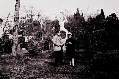 Black-and-white portrait of two adults posing beside a classical statue in a landscaped garden, likely mid-20th century. The ...