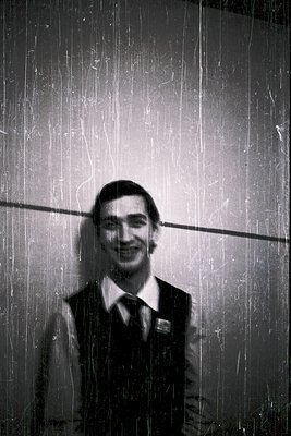 Young man in a wet, formal vest and tie under a shower of water droplets, likely from a rainstorm or fountain. Mid-20th centu...