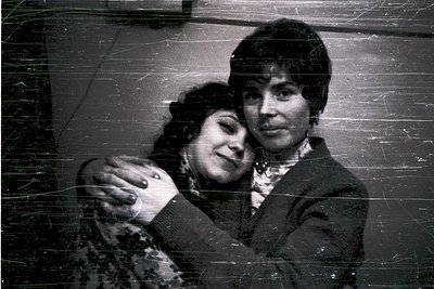 Vintage black-and-white portrait of two individuals in close embrace, likely mid-20th century (1950s–1970s). The woman wears ...