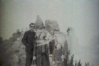 Vintage sepia-toned portrait of three generations outdoors, likely early-to-mid 20th century. Adult male in dark suit and sun...