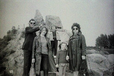 Family portrait in rugged alpine terrain, 1960s–1970s. Five individuals pose on rocky outcrops, surrounded by jagged peaks. M...