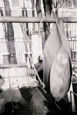 Vintage black-and-white photo of a horse-drawn carriage suspended mid-swing on a rusted metal swing set. Wrought-iron fence a...