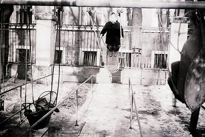 Industrial worker suspended mid-air on a crane hook in a construction site, surrounded by scaffolding and heavy machinery. Bl...