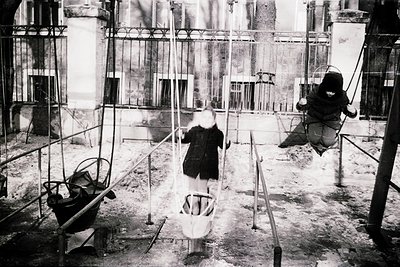 Industrial swing set in mid-20th-century factory courtyard. Three workers in protective gear (helmets, goggles) swing on make...