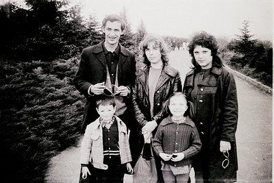 Family portrait in a wooded area, likely mid-20th century. Four adults and two children pose outdoors on a gravel path surrou...