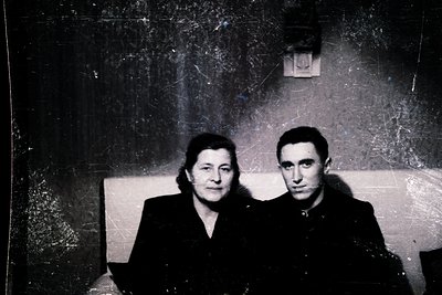 Vintage sepia-toned portrait of a man and woman seated closely on a worn sofa, likely from the 1950s–1970s. Formal attire sug...