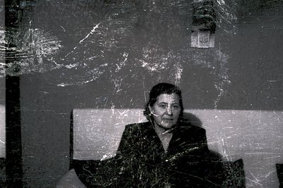 Vintage sepia-toned portrait of an elderly woman seated indoors, likely mid-20th century. She wears a structured blazer and p...