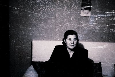 Portrait of an individual in mid-20th-century formal attire, seated against a textured wall with a wall socket. The style sug...