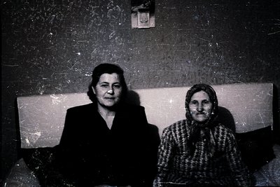 Black-and-white portrait of two women seated side-by-side against a textured wall, likely from the mid-20th century. The woma...