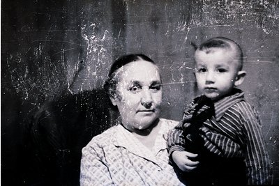 Vintage black-and-white portrait of an elderly woman holding a young child indoors, likely mid-20th century. The woman wears ...