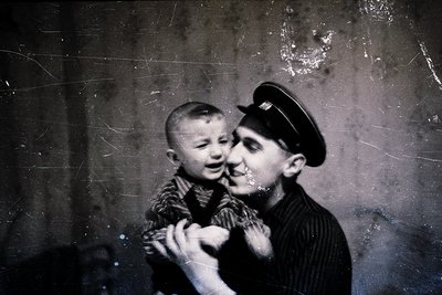 Vintage sepia-toned portrait of a man in a sailor-style cap cradling a young boy indoors, likely mid-20th century. The man’s ...