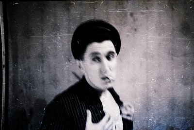 Vintage sepia-toned portrait of a man in a striped suit, holding a cigarette. Dark, textured background suggests studio light...