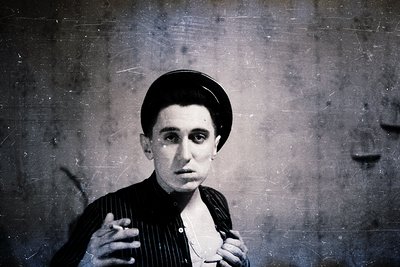 Portrait of a man in a vintage studio setting, wearing a flat cap and striped shirt. The sepia-toned image suggests a mid-20t...