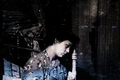 Vintage sepia-toned portrait of a woman resting her head on her hand, seated indoors. Distressed texture suggests aged photog...