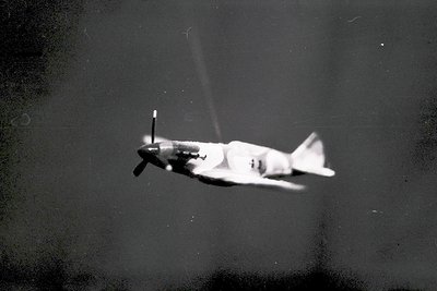 Vintage black-and-white photo of a propeller-driven military transport aircraft in mid-flight, likely a **C-47 Skytrain/Dakot...