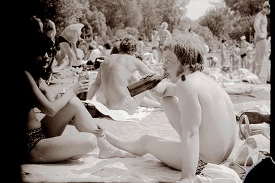Vintage black-and-white shot of a crowded beach scene with people sunbathing and relaxing on towels. Central figure, a woman ...