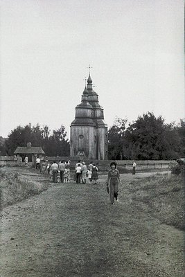 Wooden church with stepped, onion-shaped steeple in rural setting. Group of people, including children, walking toward the st...