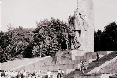 Monumental Soviet-era statue complex featuring a towering figure in profile, flanked by smaller standing figures. Engraved te...