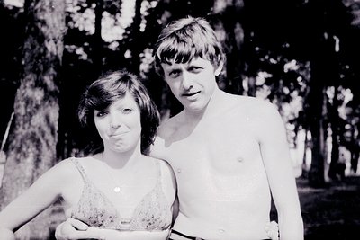 Black-and-white portrait of a man and woman in a wooded area, likely 1960s–1970s. The man wears minimalist swimwear; the woma...