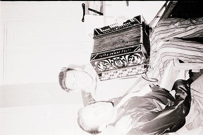 Vintage black-and-white photo of a person playing a large accordion, likely a chromatic button accordion, in an indoor settin...