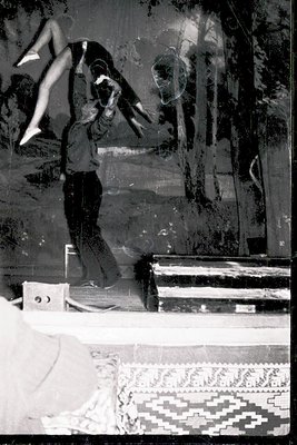 A mid-20th century dancer mid-leap against a blurred, abstract mural backdrop. The patterned floor rug suggests a studio or p...