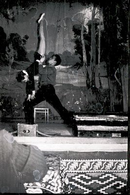 Black-and-white photo of a man performing a handstand on a wooden bench in an indoor setting, likely a gym or studio. His att...