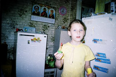 Vintage kitchen interior featuring a child holding a toy toothbrush. Brick walls display religious icons and handwritten sign...