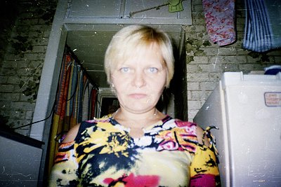 Vintage portrait of a woman in a floral-patterned blouse, framed by a brick archway and mirror. Reflections reveal shelves wi...