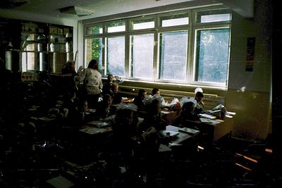 Vintage classroom with mid-century design—wooden desks, chalkboards, and large windows letting in natural light. Students sea...