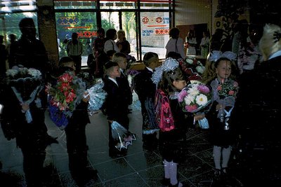 First-day-of-school ceremony in a Soviet-era school building, likely Bulgaria (). Children in formal attire—girls in embroide...