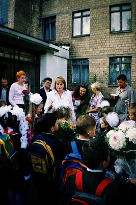 School graduation ceremony in Eastern Bloc-era building, likely 1970s–1980s. Students in formal attire—white blouses, ties, a...