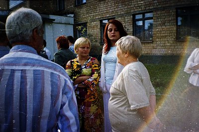 Vintage group photo in a residential courtyard, featuring adults in 1970s-80s attire—striped shirts, floral dresses, and patt...