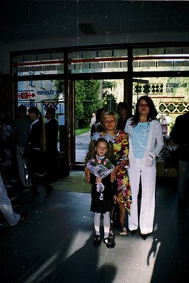 Vintage indoor shot of three women posing near a glass entrance with Cyrillic signage. The woman in white pantsuit holds a yo...