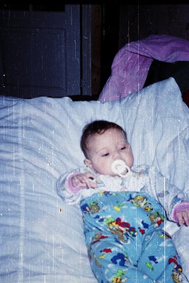 A tranquil infant sleeps peacefully in a crib, swaddled in a floral-patterned onesie and a pacifier in mouth. Raindrops strea...
