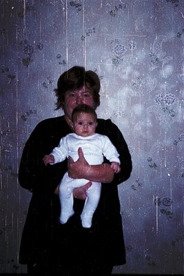 Vintage portrait of an adult holding a baby indoors, likely mid-20th century. The woman wears a dark, high-neck garment, whil...