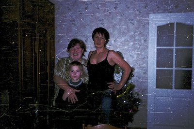 Family portrait reflected in a frosted window, capturing a festive moment. Two adults and a child pose indoors near a decorat...