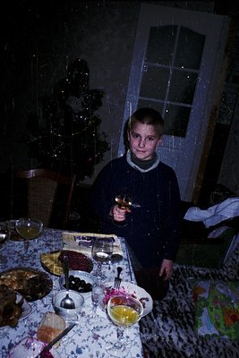Vintage indoor holiday scene featuring a young boy in a dark sweater holding a toy pistol, posed beside a festively decorated...