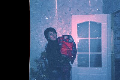 Vintage black-and-white photo of two children hugging through a frosted window, snowflakes visible on glass. Indoor setting w...