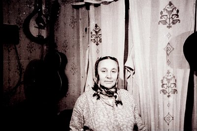 Vintage black-and-white portrait of an elderly woman in traditional Eastern European attire, featuring a headscarf and embroi...