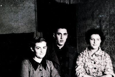 Black-and-white portrait of three individuals in formal attire, likely mid-20th century (1940s–1950s). Centered figure wears ...
