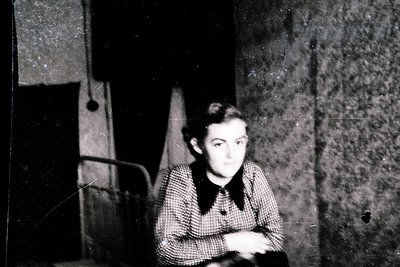 Vintage black-and-white portrait of a young individual seated indoors, likely mid-20th century. Checkered sweater and dark ha...