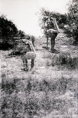 Black-and-white rural scene depicting manual labor in agricultural construction, likely mid-20th century. Two men and a child...