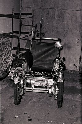 Vintage sidecar motorcycle with exposed engine and dual headlamps, parked in an industrial garage. Sidecar features a simple ...